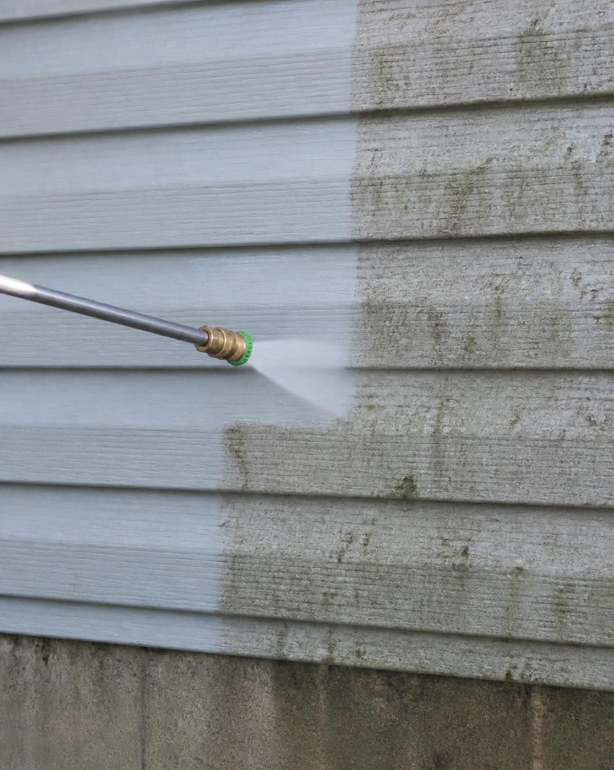 Pressure washer stripping grey algae from concrete, half clean and half dirty
